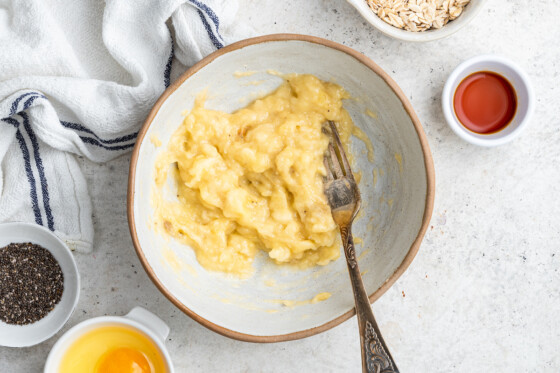 A mashed banana in a white bowl with a metal fork.