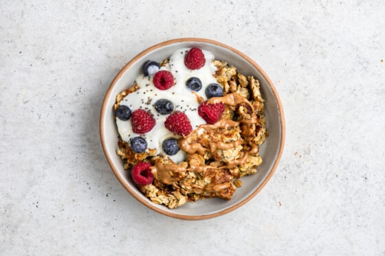 A bowl of scrambled oats with a scoop of yogurt, chia seeds, fresh berries, and a drizzle of almond butter on top.