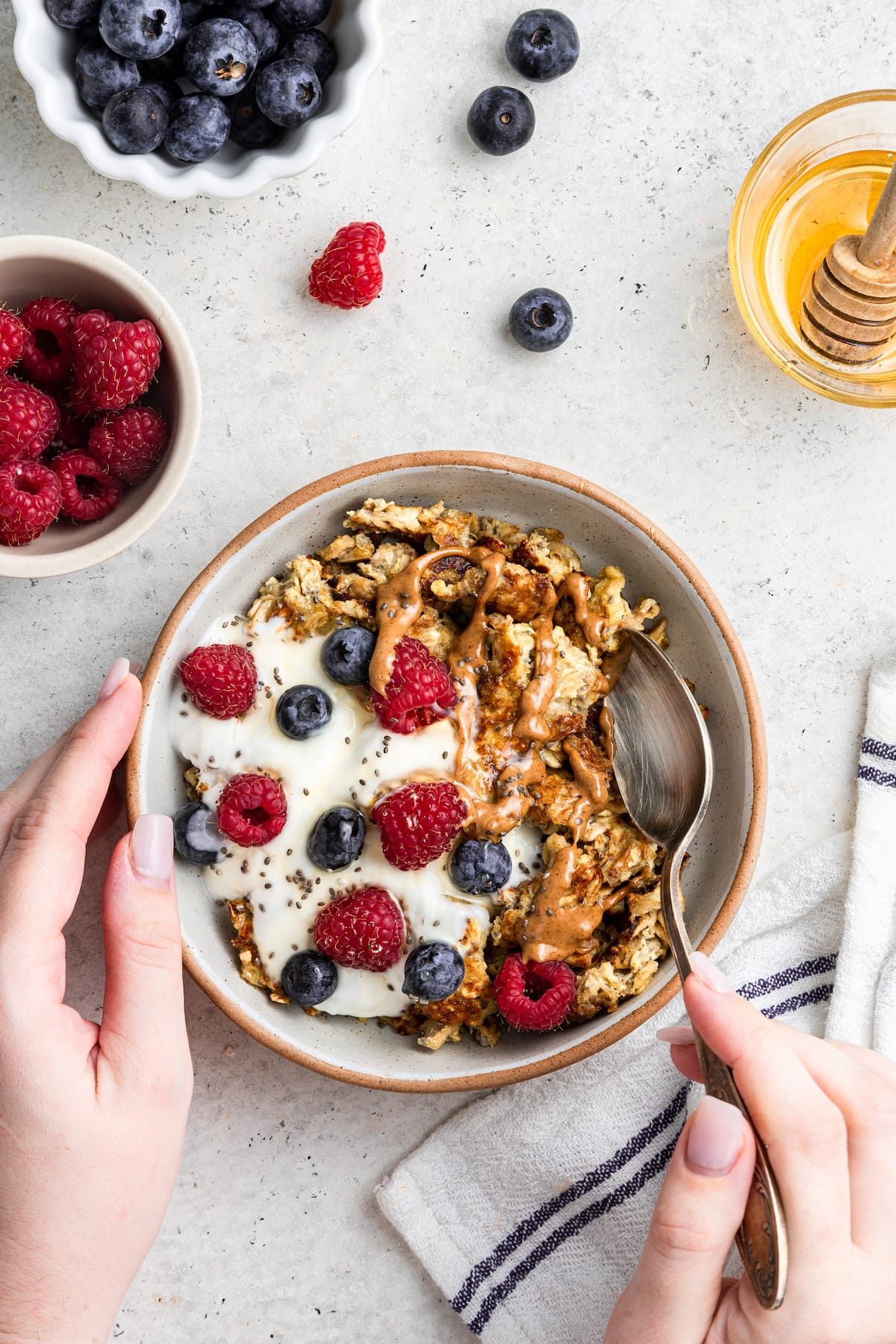 Woman's hand holding a metal spoon that is going into a bowl of scrambled oats.