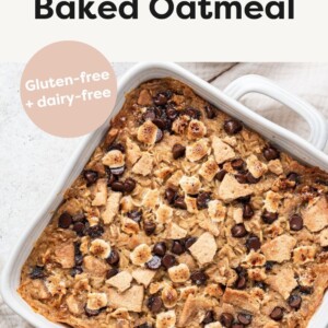 A white square baking dish with the s'mores baked oatmeal inside after baking in the oven. The top is lightly browned with chocolate chips, mini marshmallows, and crushed graham crackers.