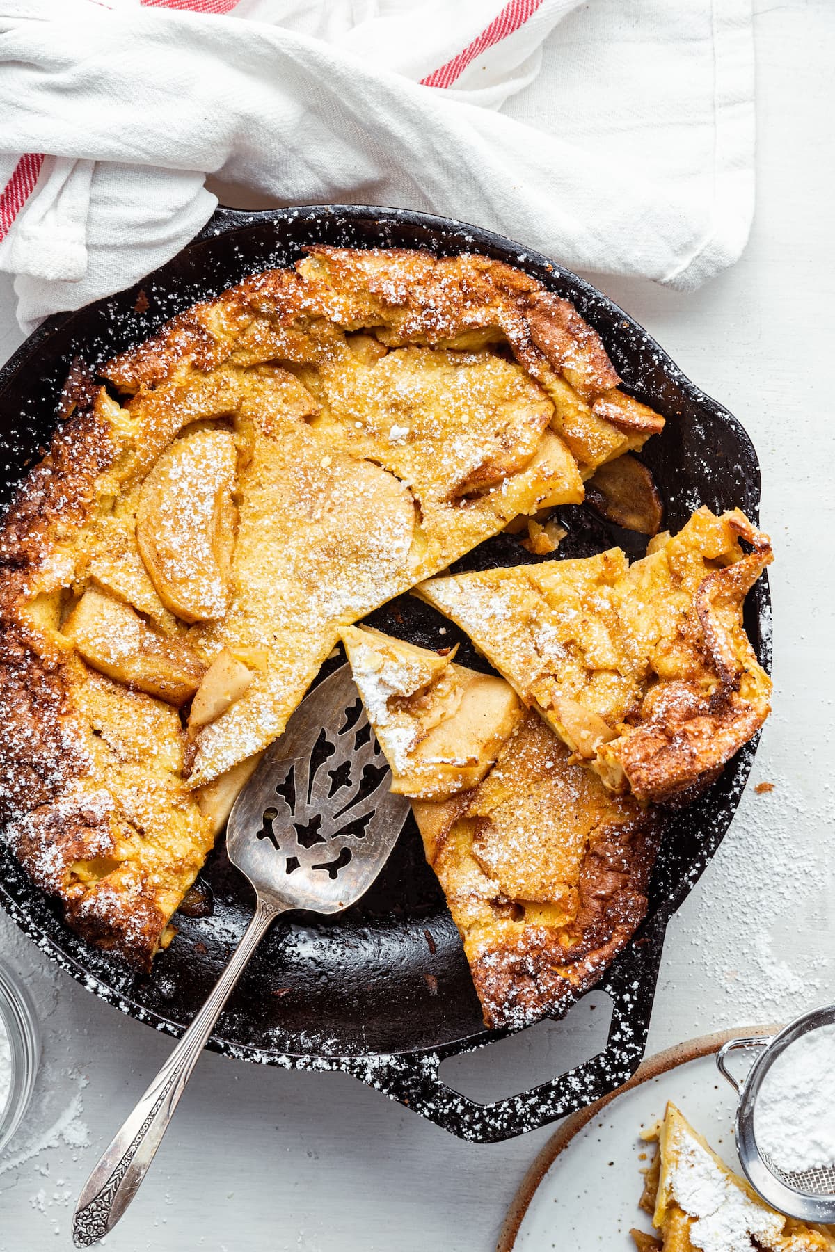 Apple dutch baby sliced in a cast iron pan with a serving spatula.