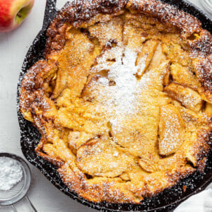 A cooked apple dutch baby in a cast iron with powdered sugar sprinkled on top.