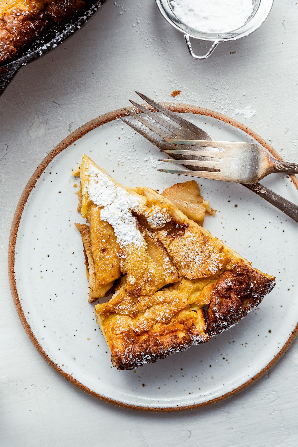 A piece of apple dutch baby on a plate served with forks.