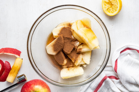 Sliced apples with cinnamon and maple syrup in a clear mixing bowl.