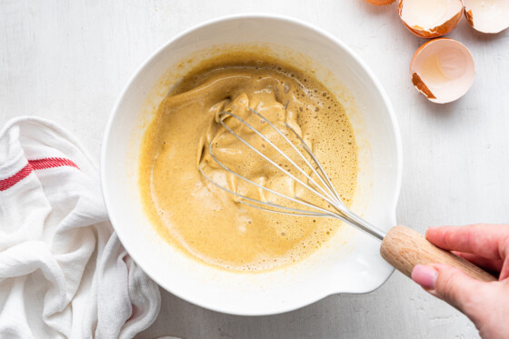 A woman's hand whisking together the wet ingredients for the apple dutch baby.