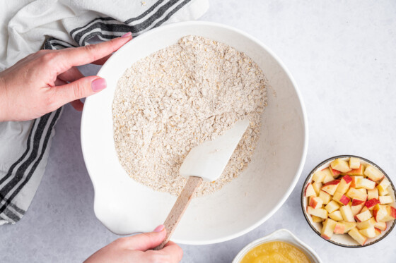 A woman's hand with a silicon spatula in a large mixing bowl of blended oats.