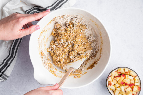 A woman's hand using a silicone spatula to mix ingredients for the apple oatmeal bars in a large mixing bowl.