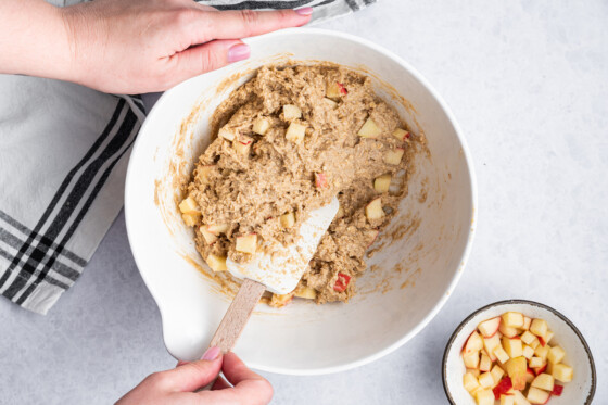 A woman's hand using a silicone spatula to mix ingredients for the apple oatmeal bars in a large mixing bowl.