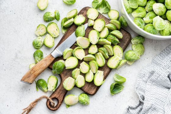 Halved Brussels sprouts on a cutting board with a knife.