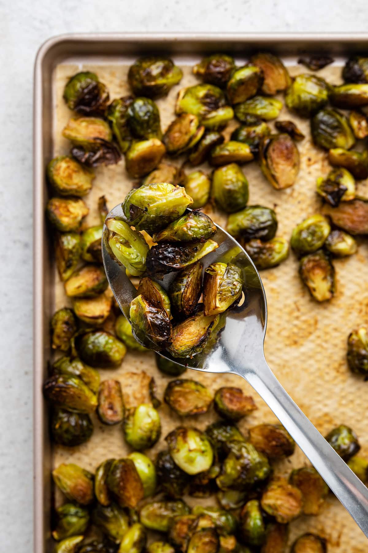 Balsamic Brussels Sprouts on a baking tray with a large metal serving spoon holding a spoonful of them.