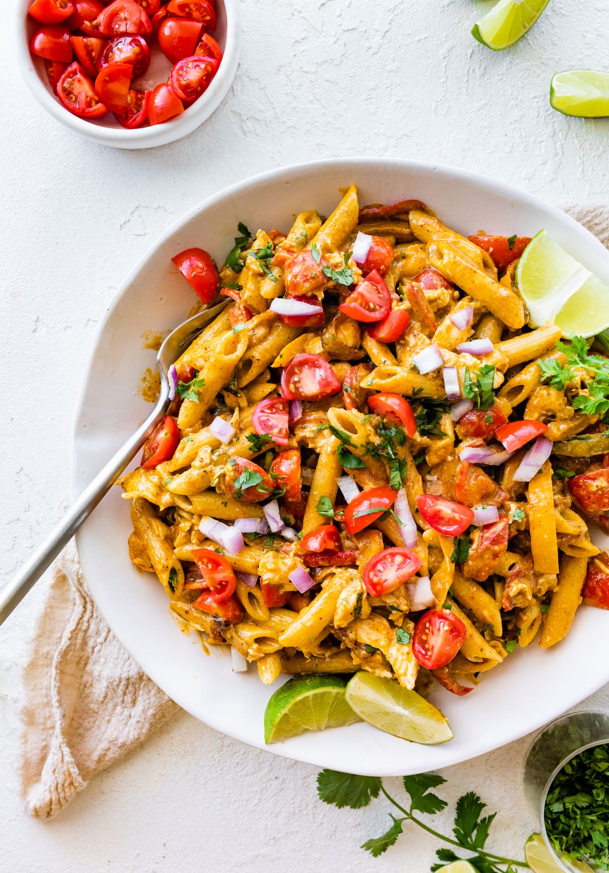 A white bowl with chicken fajita pasta salad and lime slices on the side.