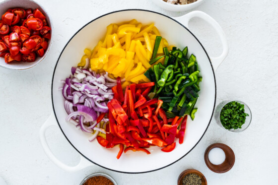 Fresh onion and yellow, red, and green bell peppers in a large white pot.