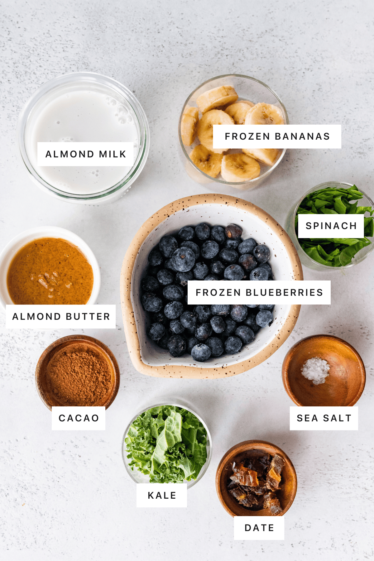 Ingredients for the chocolate blueberry smoothie: frozen bananas, frozen blueberries, almond milk, almond butter, cacao powder, kale, spinach, date and sea salt.