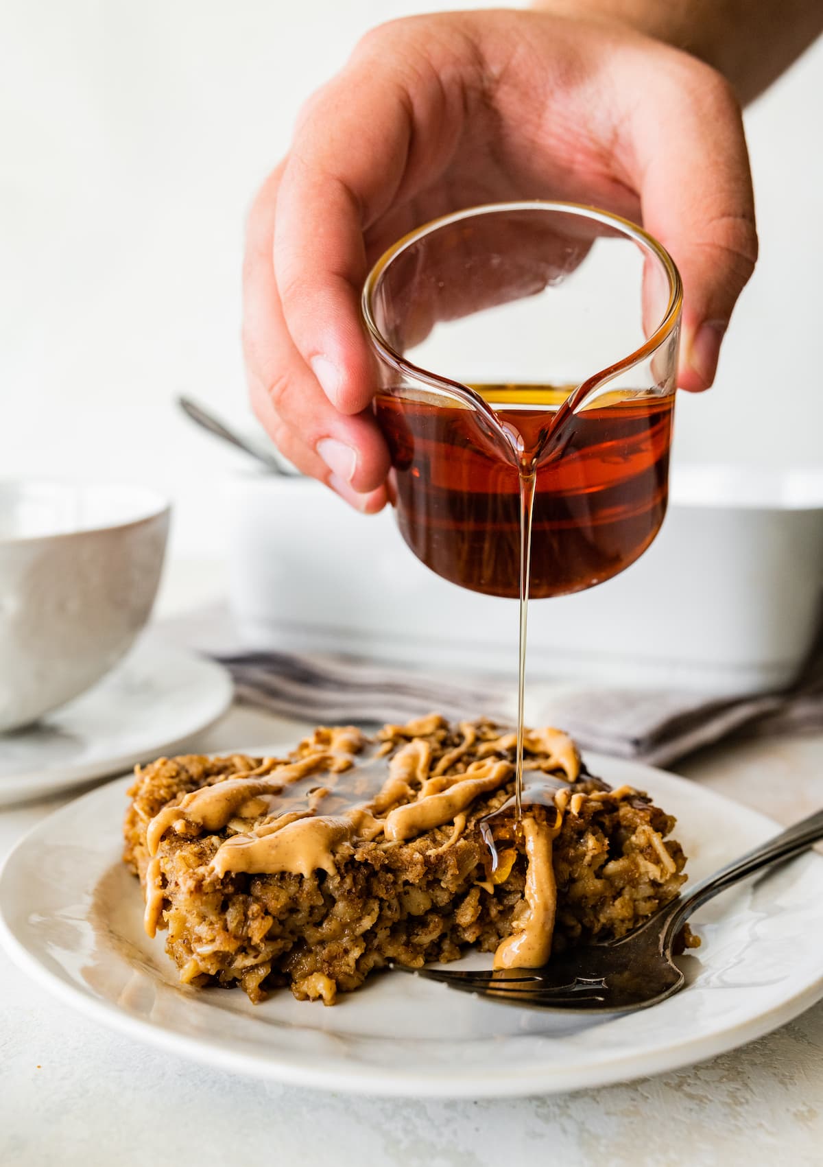 A hand pouring syrup over a piece of coffee baked oatmeal on a small plate.