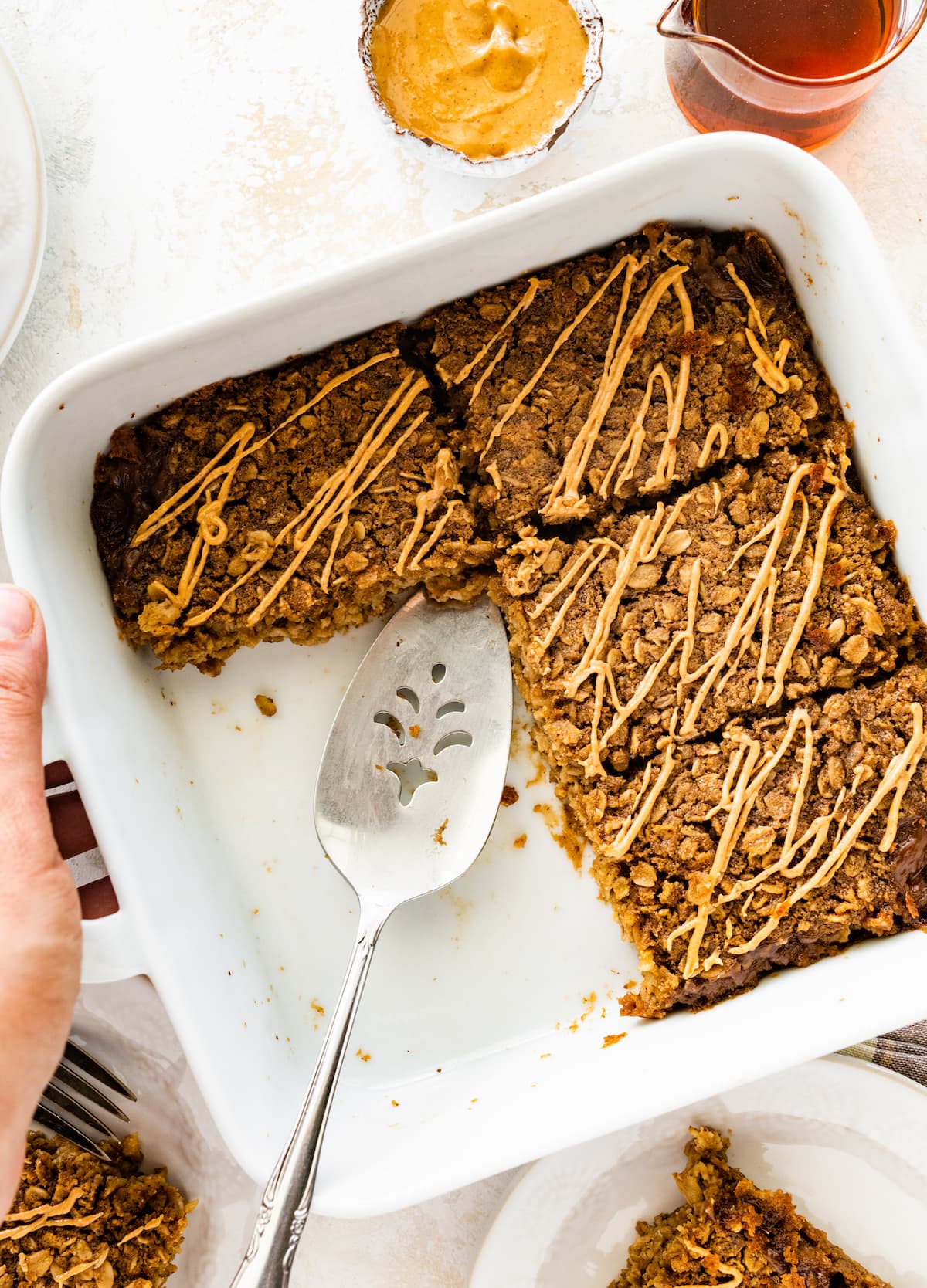 Coffee baked oatmeal with a metal serving spatula in a square baking dish and topped with a drizzle of nut butter.