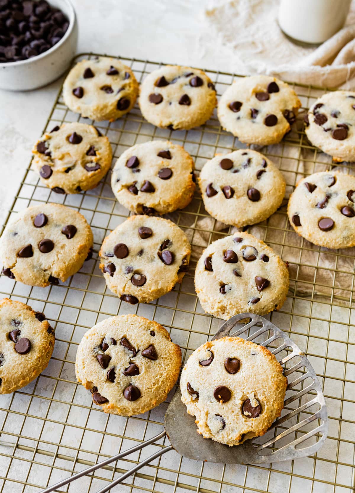 Cottage cheese chocolate chip cookies on a metal cooling rack with one cookie on a metal spatula.