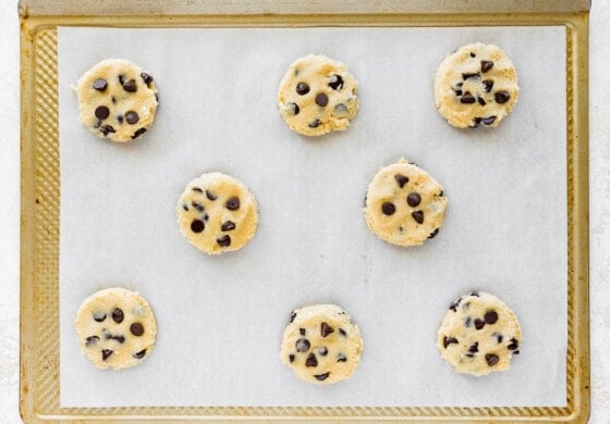 Eight cottage cheese chocolate chip cookies on parchment paper, on a baking tray before being baked.