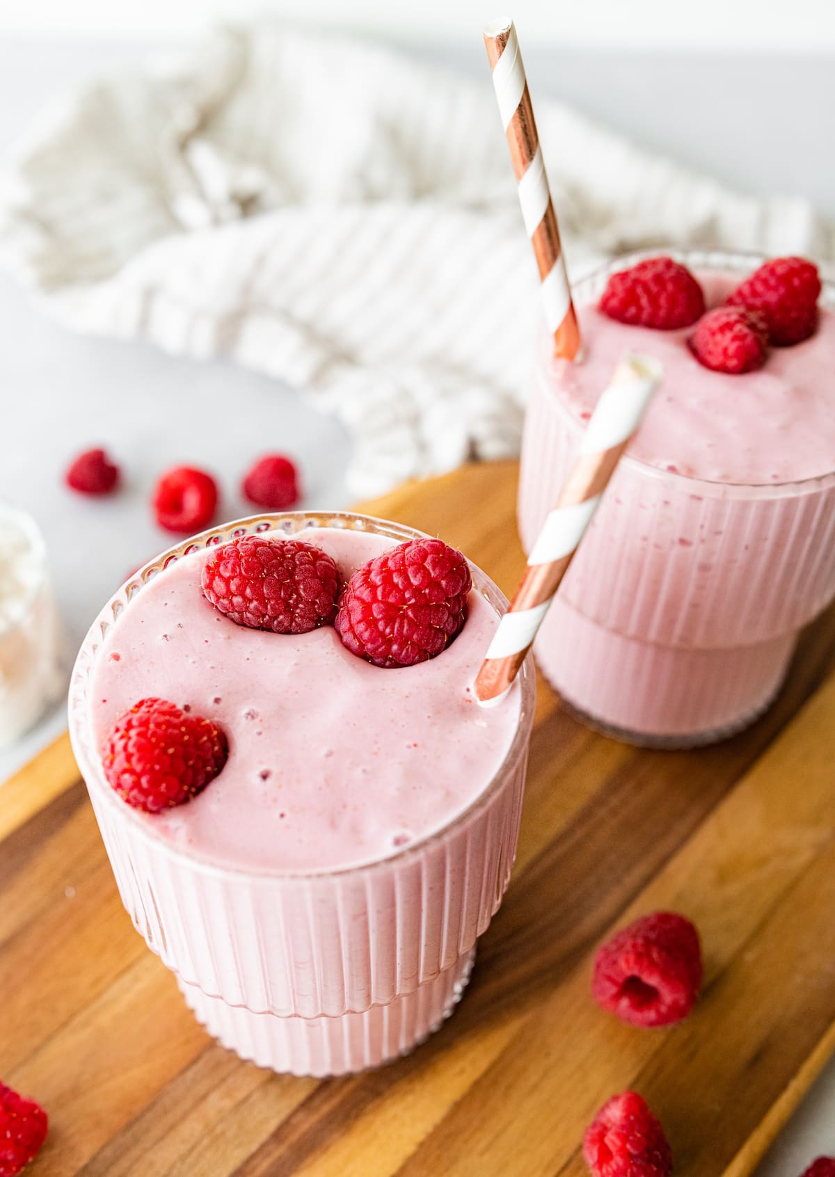 Two cottage cheese smoothies with straws, topped with fresh raspberries.