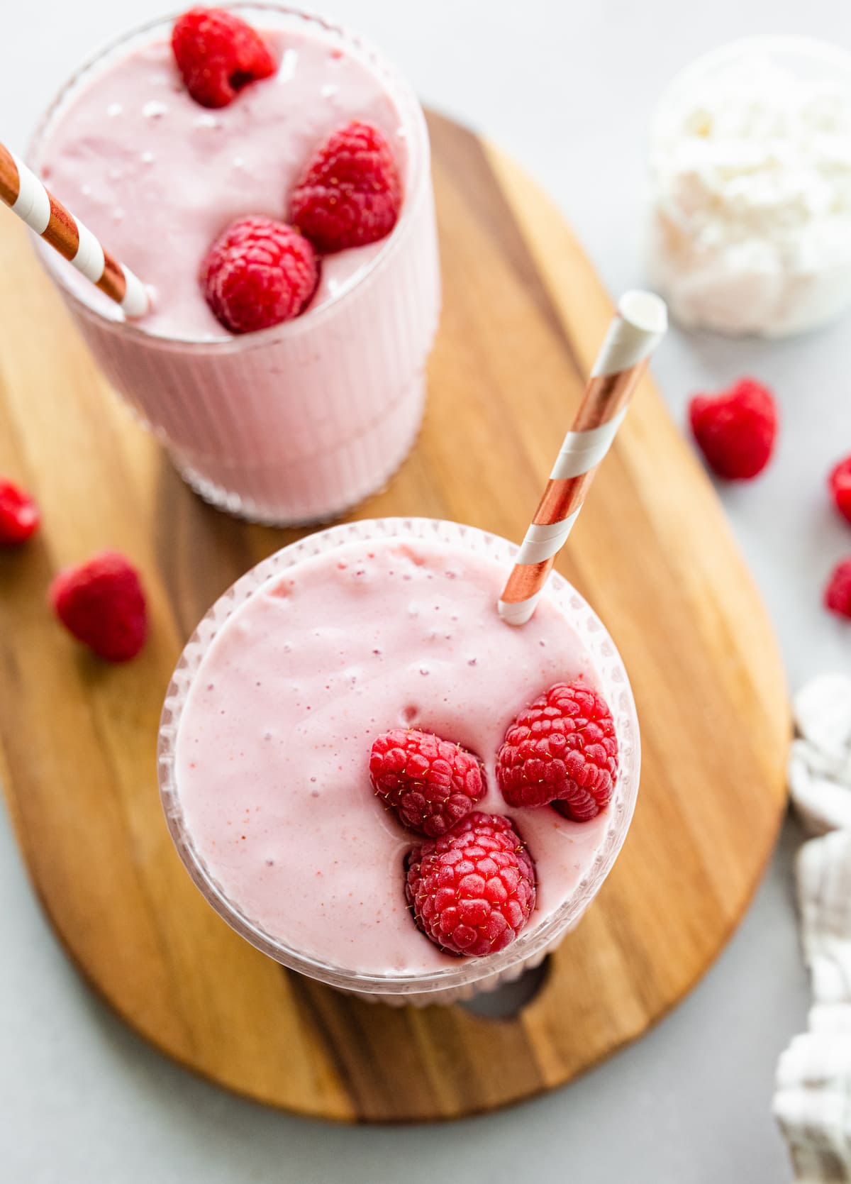 Two cottage cheese smoothies with straws, topped with fresh raspberries.