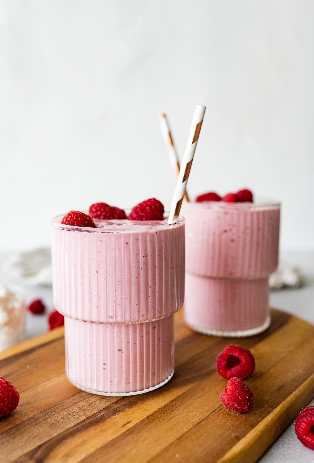 Two cottage cheese smoothies with straws, topped with fresh raspberries.