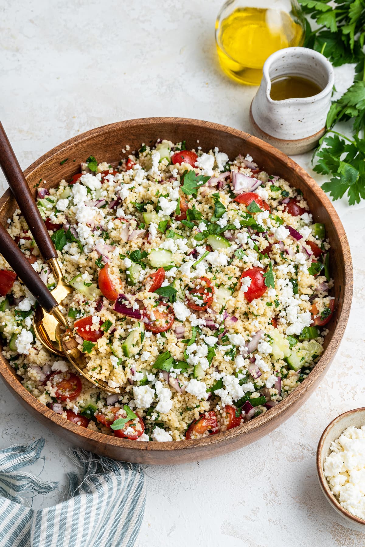 Couscous salad in a large wooden bowl with two serving spoons.