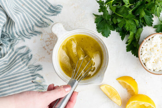 Woman's hand using a metal whisk in a small bowl with a lemon dressing.