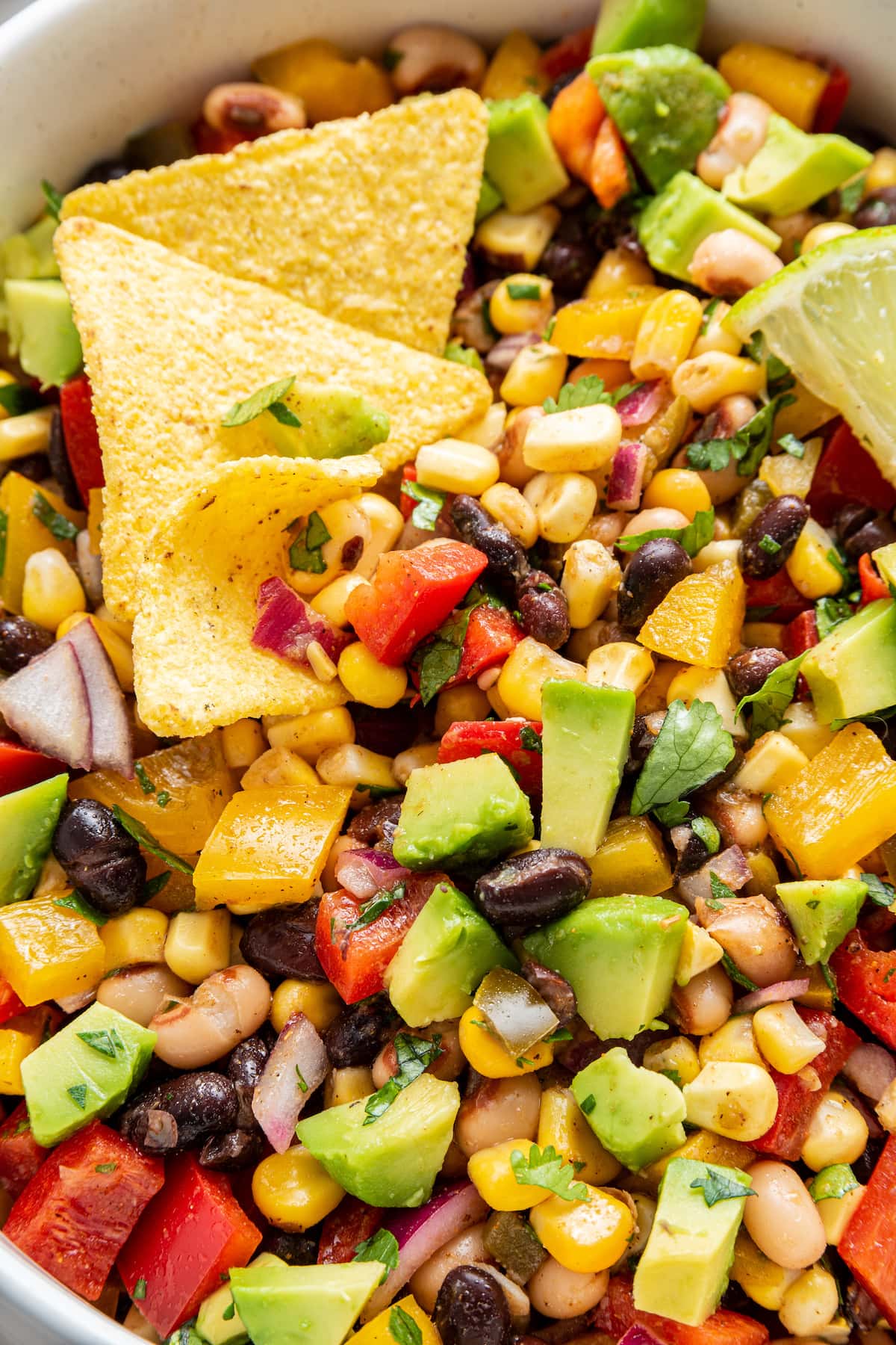 Cowboy caviar in a white bowl with diced avocado, a lime wedge, and tortilla chips.