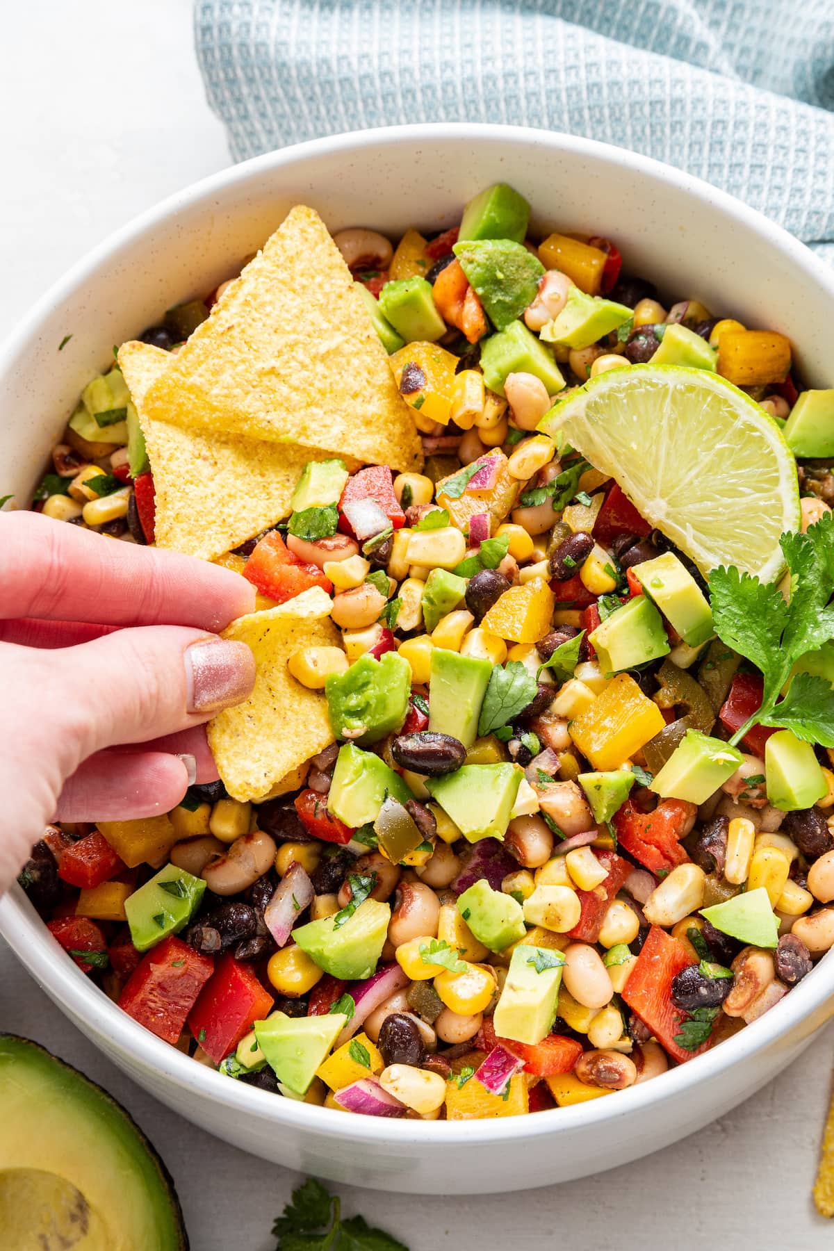 A woman's hand using a tortilla chip to scoop up some cowboy caviar in a bowl.