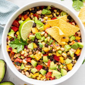 Cowboy caviar in a white bowl with diced avocado, a lime wedge, and tortilla chips.