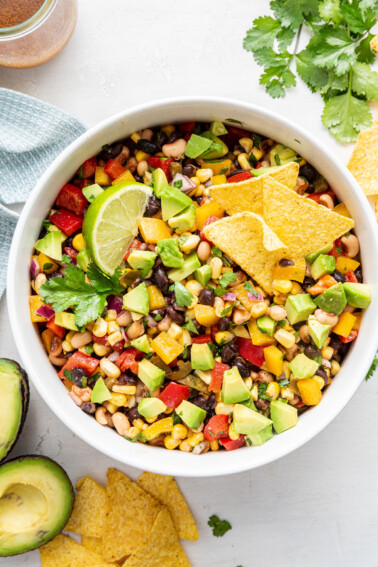 Cowboy caviar in a white bowl with diced avocado, a lime wedge, and tortilla chips.