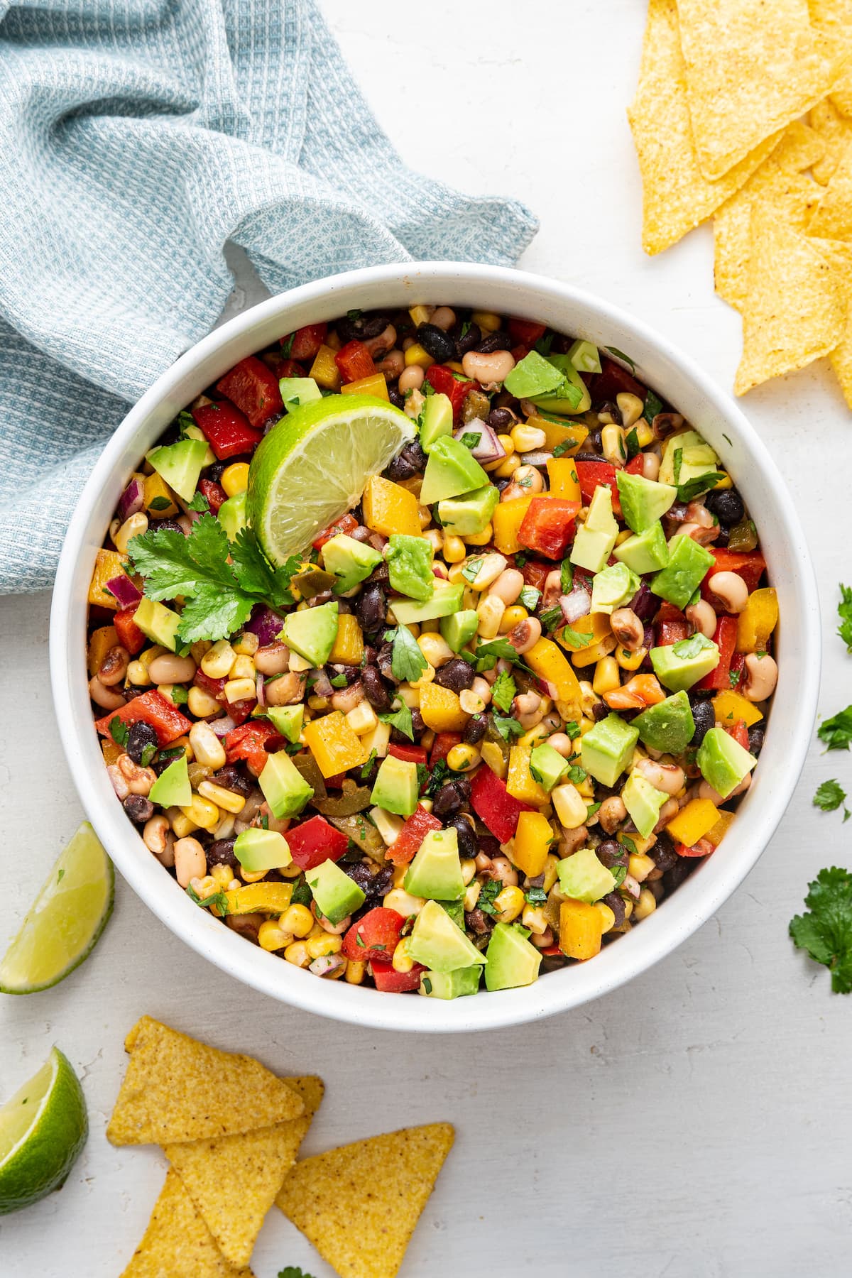Cowboy caviar in a white bowl with diced avocado, a lime wedge, and tortilla chips on the side.