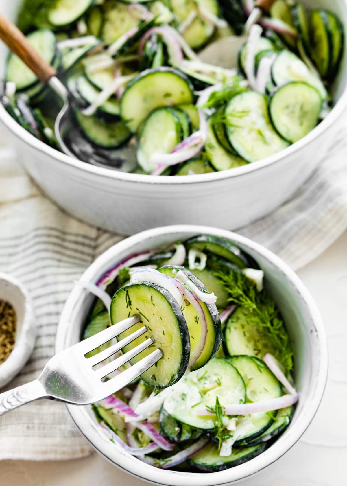 A fork taking a bite-size portion of cucumber salad from a bowl.