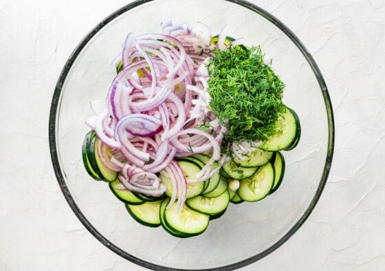 Ingredients for the creamy cucumber salad. Noticeable ingredients are sliced cucumber, red onion, and fresh dill.