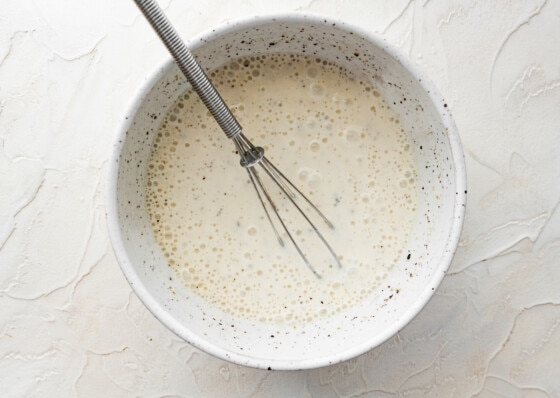 A yogurt based dressing in a white bowl with a metal whisk.
