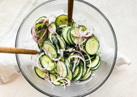 Creamy cucumber salad in a large glass bowl with two serving spoons.
