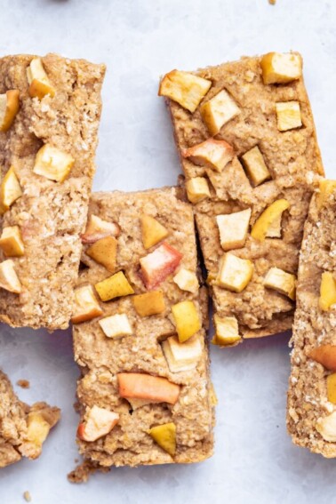 Four apple oatmeal bars near one another on a white counter top.