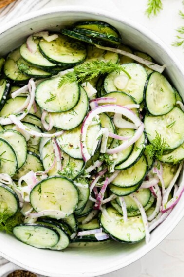 Creamy cucumber salad in a large white bowl.