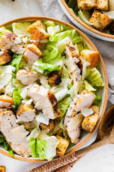 Grilled chicken Caesar salad in a bowl with two wooden serving spoons nearby.