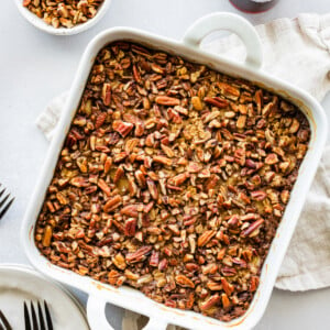 Baked oatmeal topped with chopped nuts in a white square baking dish.