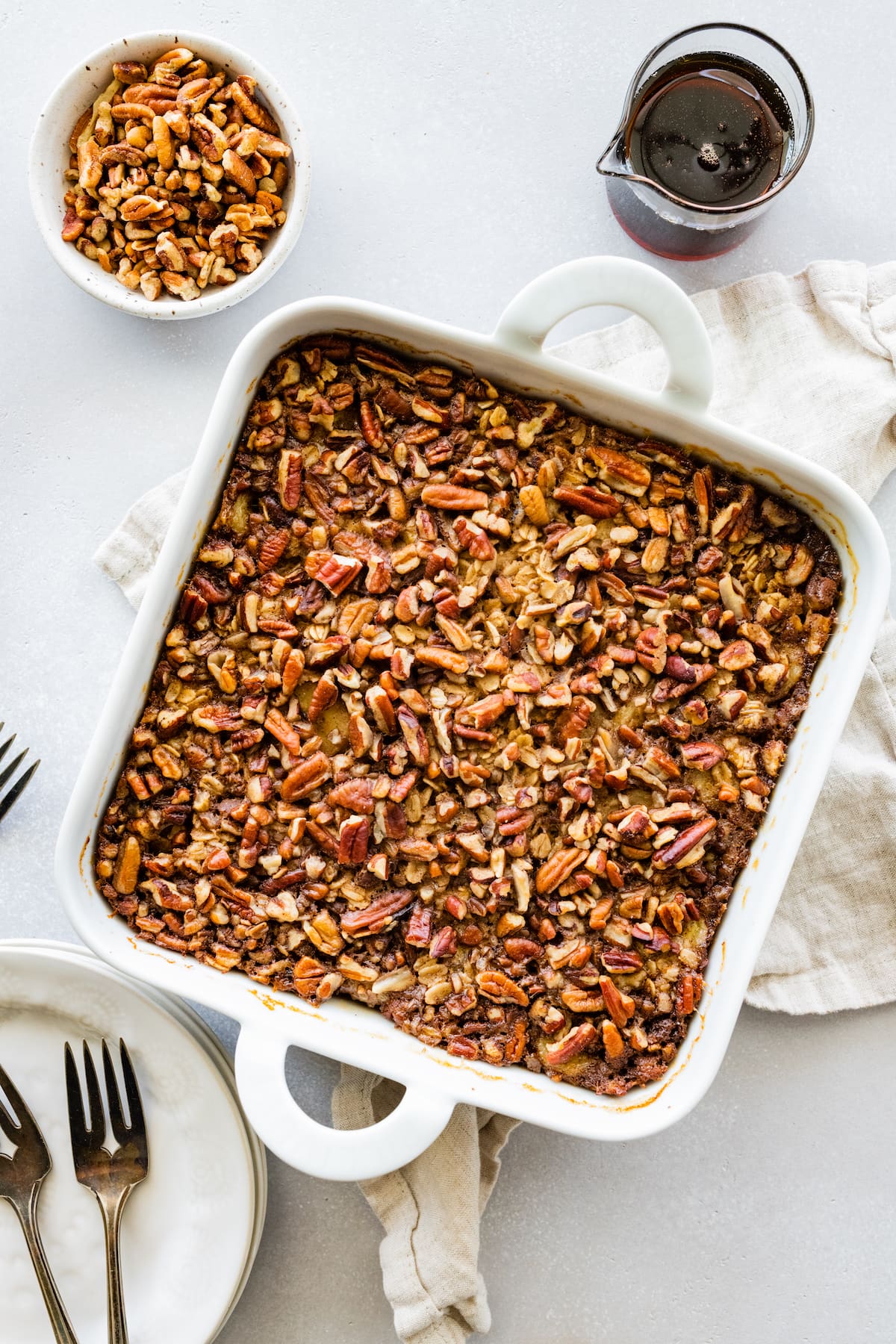 Baked oatmeal topped with chopped nuts in a white square baking dish.