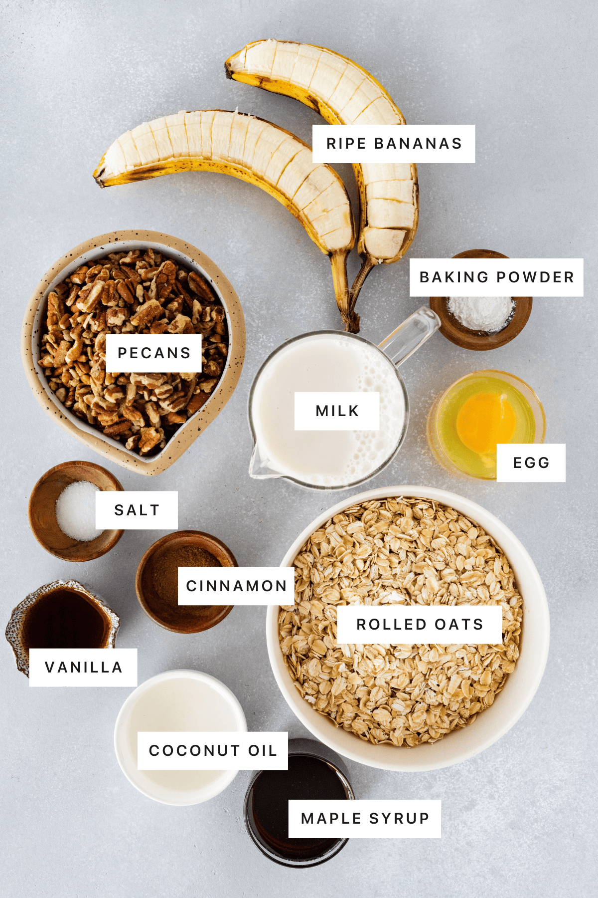 Ingredients for baked oatmeal: bananas, pecans, milk, egg, baking powder, rolled oats, maple syrup, coconut oil, cinnamon, vanilla and salt.