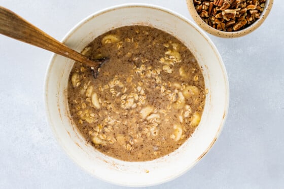 Baked oatmeal batter mixed together in a white bowl with a wooden spoon.