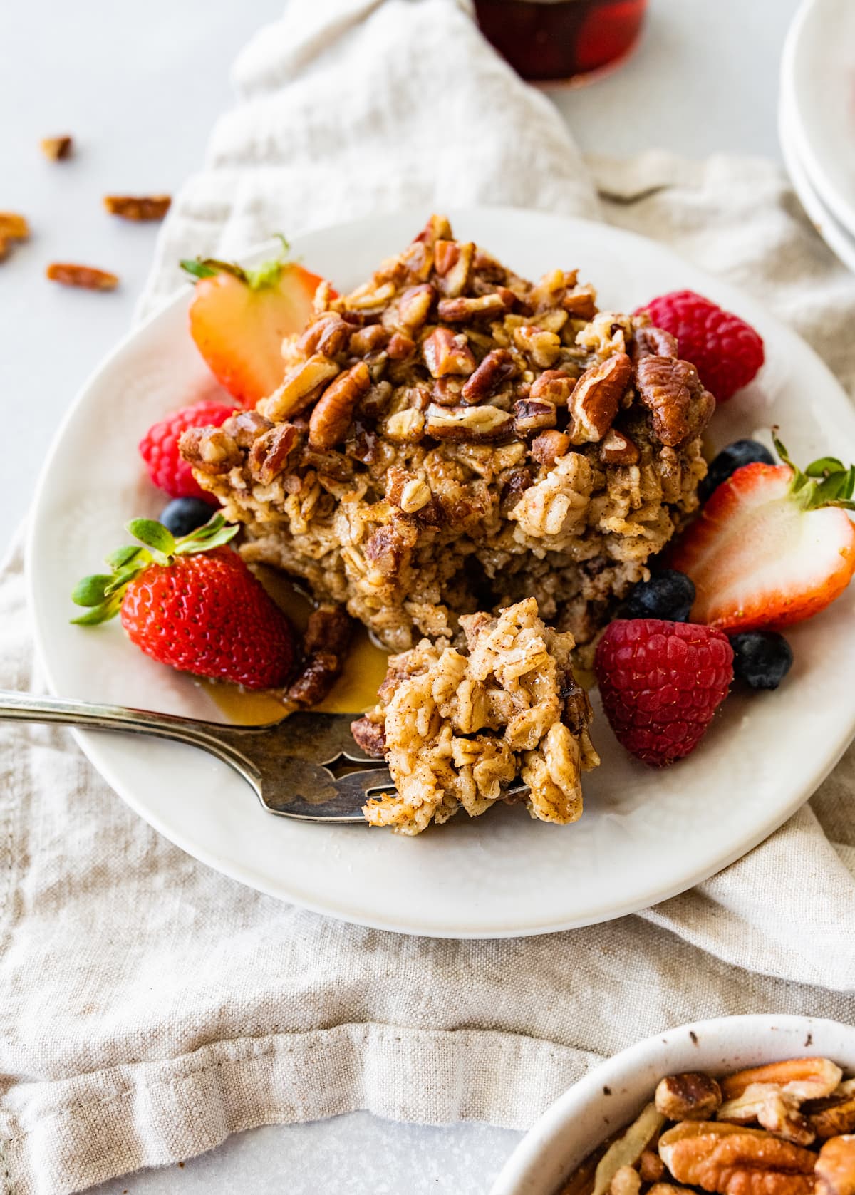 A slice of baked oatmeal served on a white plate alongside fresh berries.