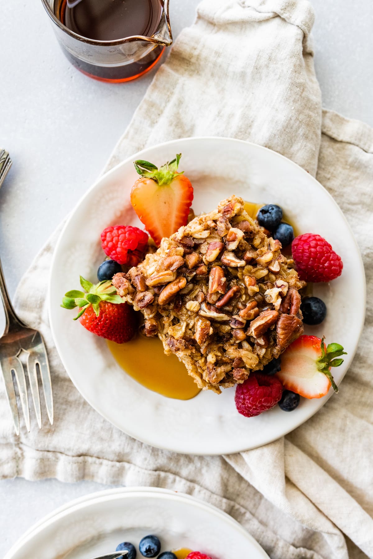 A slice of baked oatmeal served on a white plate with maple syrup and fresh berries.