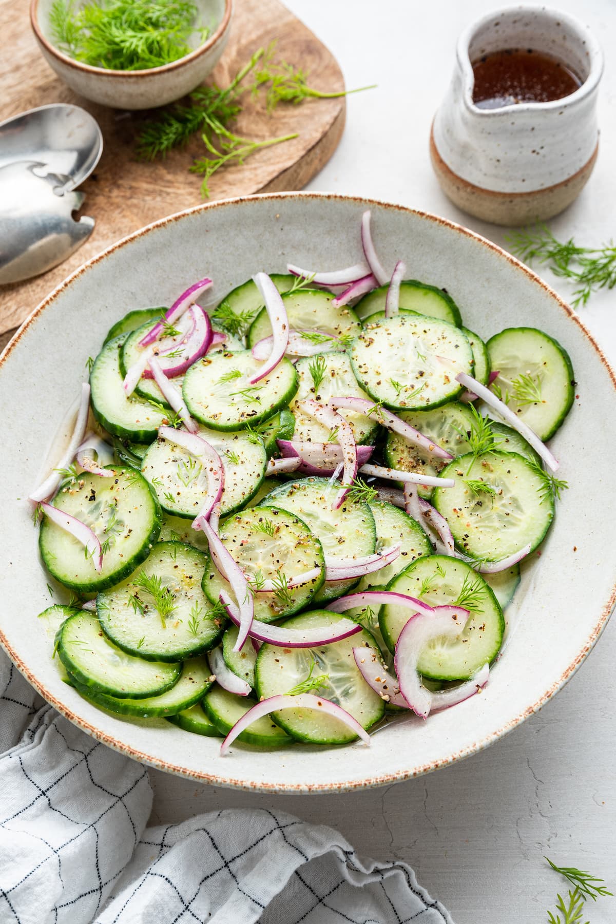 Cucumber salad in a white bowl with cucumber slices, red onion and vinaigrette.