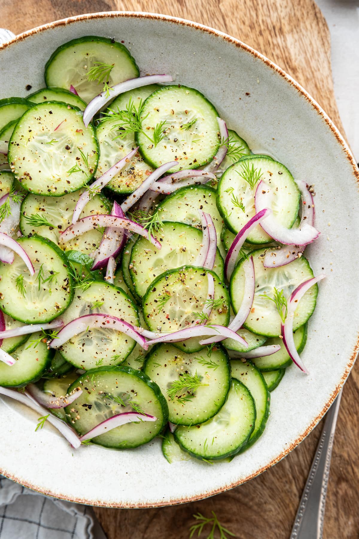 Cucumber salad in a white bowl with cucumber slices, red onion and vinaigrette.