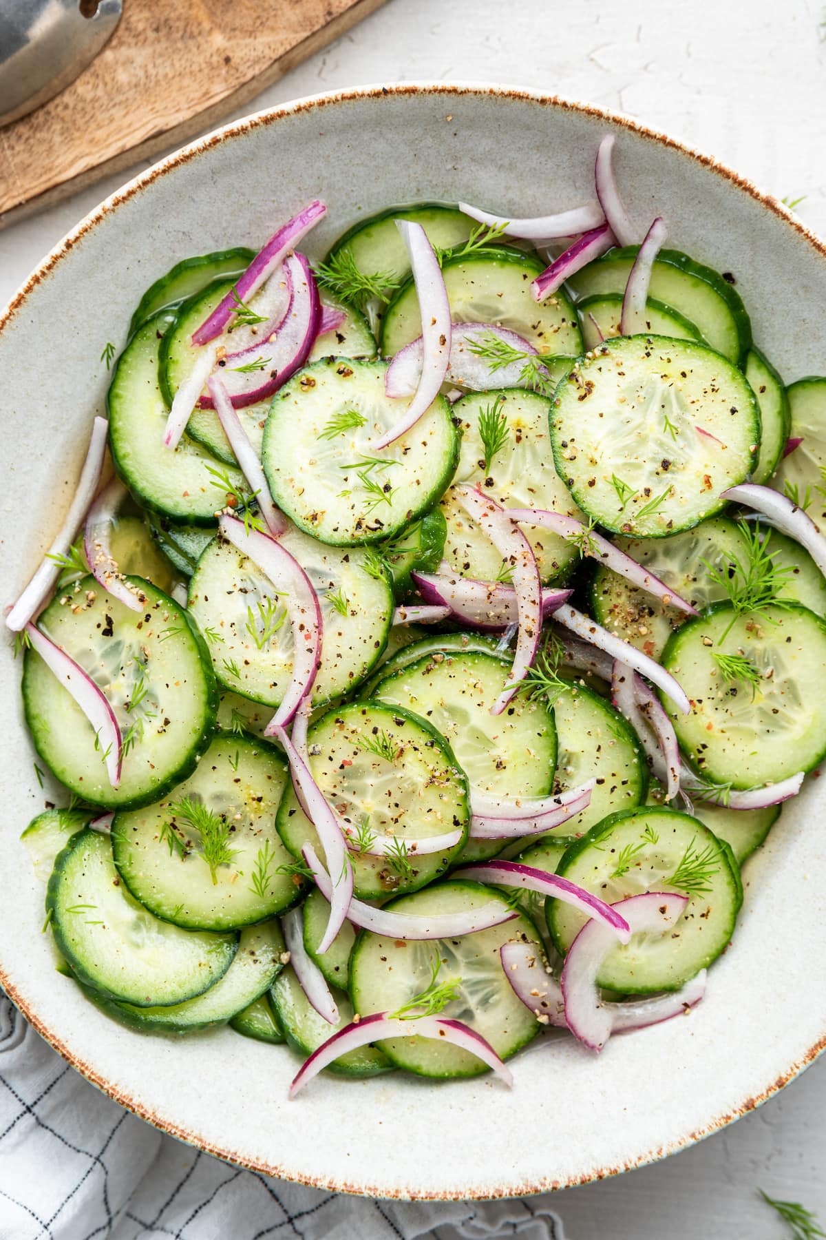 A cucumber salad in a white bowl with sliced cucumbers, red onion, and a vinaigrette.
