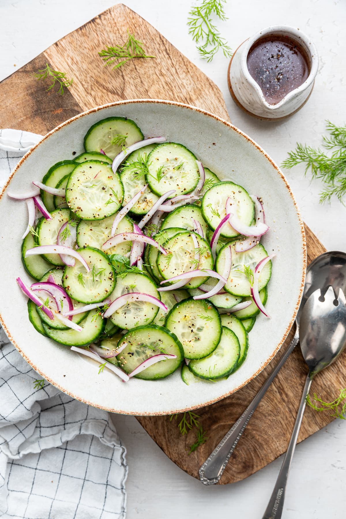 A cucumber salad in a large white bowl on a wood cutting board.