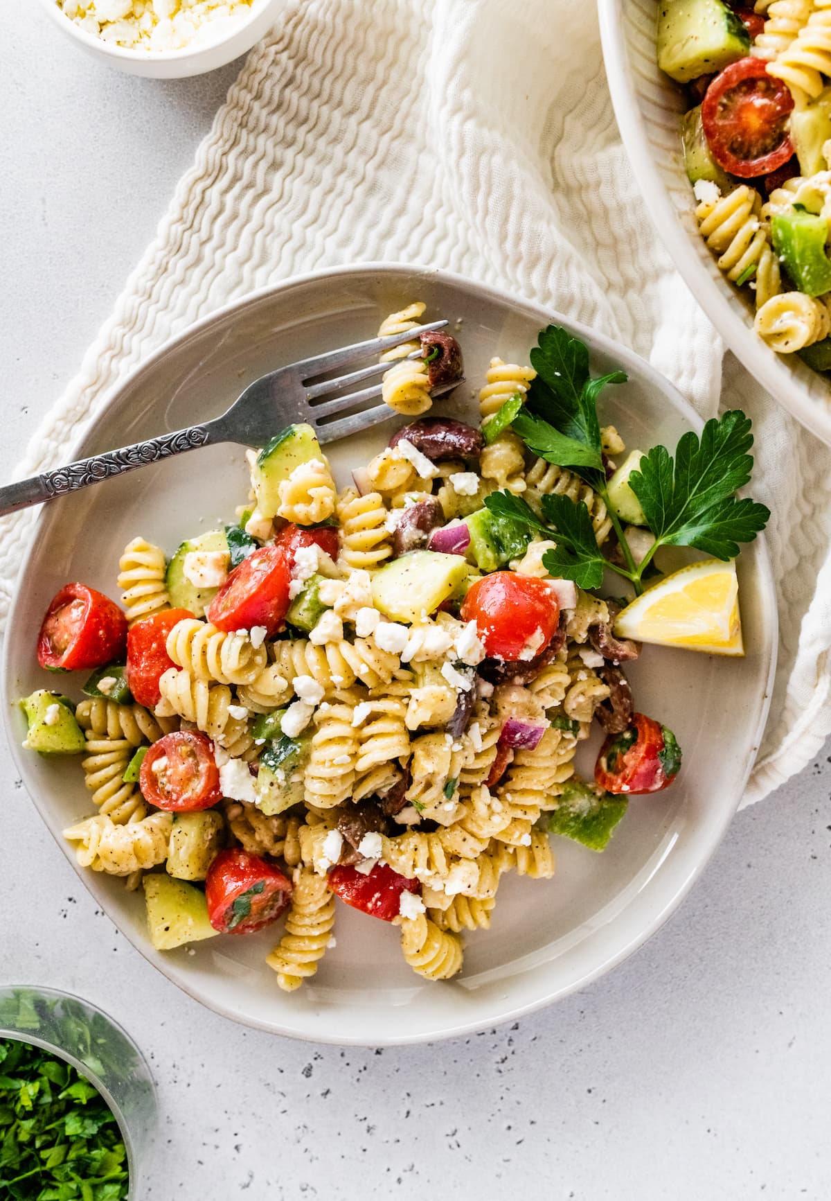 A serving of greek pasta salad on a plate with a metal fork.