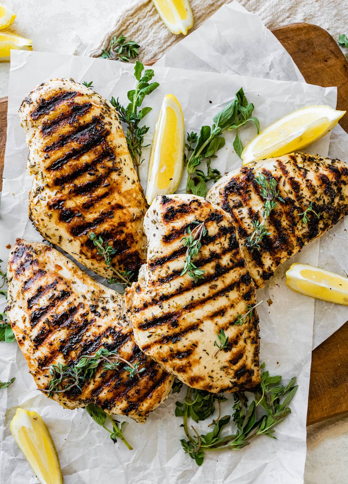 Four grilled chicken breasts on parchment paper with fresh herbs and lemon slices.